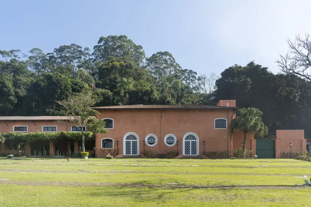 Fachada da capela do Parque dos Ipês, com janelas em arco, telhado de barro e gramado aberto.