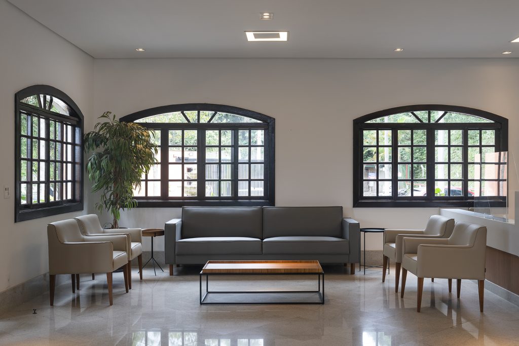 Sala de espera do Parque dos Ipês, com sofá, janelas em arco e planta ornamental