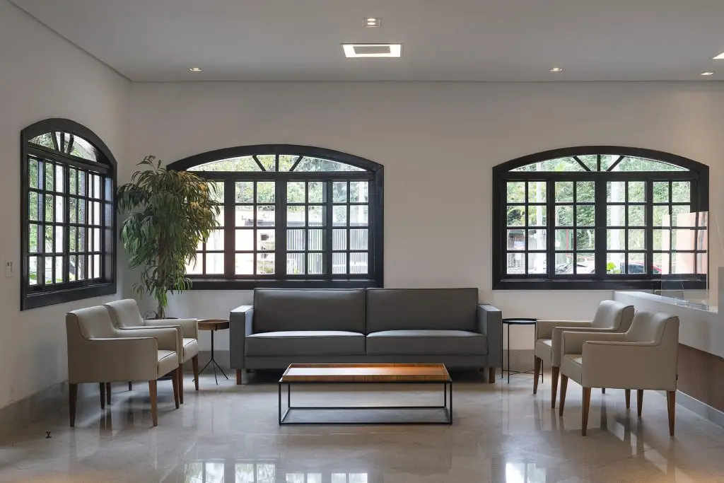 Sala de espera do Parque dos Ipês, com sofá, janelas em arco e planta ornamental